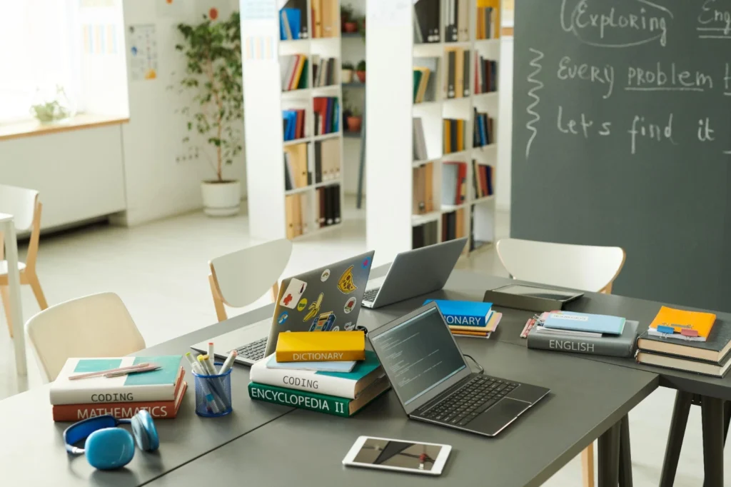 Modern study desk with laptops, tablets, textbooks on coding, mathematics, and english, with headphones and stationery.